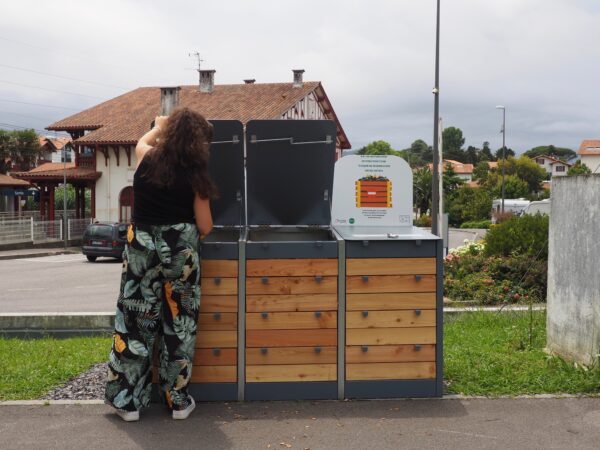 Composteur de chez Abriplus en acier et bois, avec signalétique et une personne devant